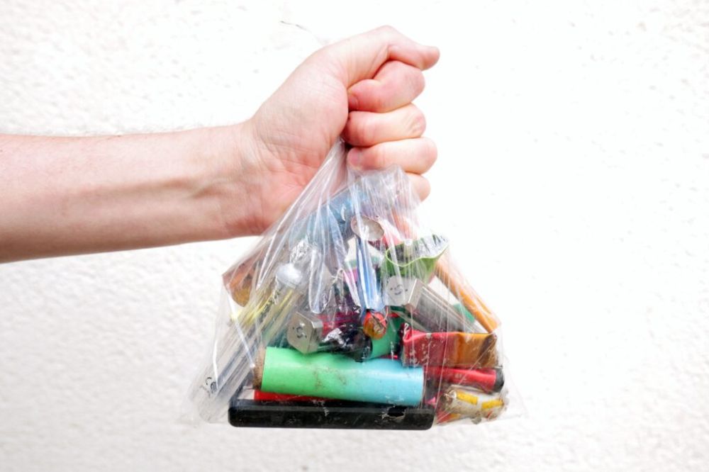 An image of a human hand holding a clear plastic bag with vapes that are intended for disposal